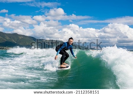 Wakesurfing. Young woman in wetsuit learning to wakesurf on the sea. Athletic female riding the waves on sunny day. Watersport concept. Royalty-Free Stock Photo #2112358151