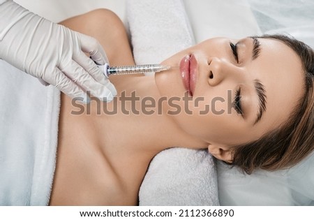 Woman while procedure lip augmentation at cosmetology clinic with beautician. Filler injection for beautiful female lips augmentation with hyaluronic, top view Royalty-Free Stock Photo #2112366890