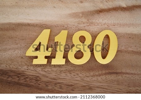 Wooden Arabic numerals 4180 painted in gold on a dark brown and white patterned plank background.