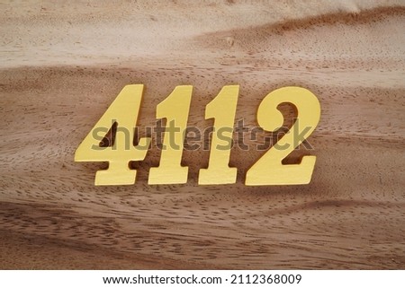 Wooden Arabic numerals 4112 painted in gold on a dark brown and white patterned plank background.