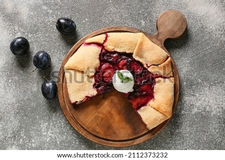Board with tasty homemade plum galette on grunge background