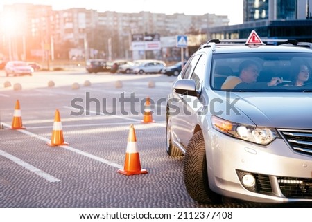 Driving Test. Training parking. Cones for the examination, driving school concept. Young woman steer car with the steering wheel, maybe she has a driving test perhaps she exercises the parking. Royalty-Free Stock Photo #2112377408