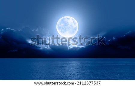 Night sky with big blue moon rises above the sea among the clouds "Elements of this image furnished by NASA"