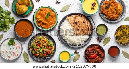 Indian ethnic food buffet on white concrete table from above: curry, samosa, rice biryani, dal, paneer, chapatti, naan, chicken tikka masala, mango lassi, dishes of India for dinner background Royalty-Free Stock Photo #2112379988