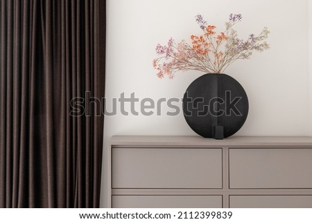 Dried colourful spring flowers in black hand glazed ceramic vase in nordic style against white wall. Minimal interior decoration concept