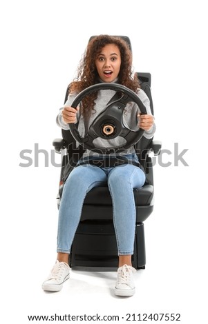 Shocked young African-American woman with steering wheel in car seat on white background Royalty-Free Stock Photo #2112407552