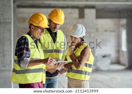 Three caucasian engineers discussing over digital tablet on the construction site Royalty-Free Stock Photo #2112413999