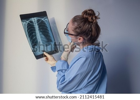 Doctor is looking at xray of lungs and thinking. Female lung specialist in glasses examining MRI or computer tomography picture. Covid diagnostics concept. Work of radiologist.