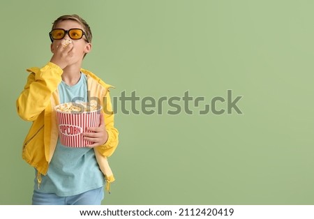 Little boy in eyeglasses eating tasty popcorn on green background