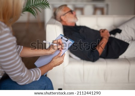 Depressed mature man lies on a sofa at a session with a psychologist. Senior patient with problems. Royalty-Free Stock Photo #2112441290