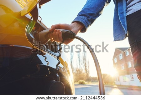Electric car plugged in outside house on street with a sunset Royalty-Free Stock Photo #2112444536