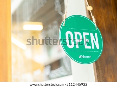 Open sign hanging on the entrance door. Close up of OPEN WELCOME notice sign board label hanging through glass door front shop. Business open back to new normal after coronavirus disease concept.