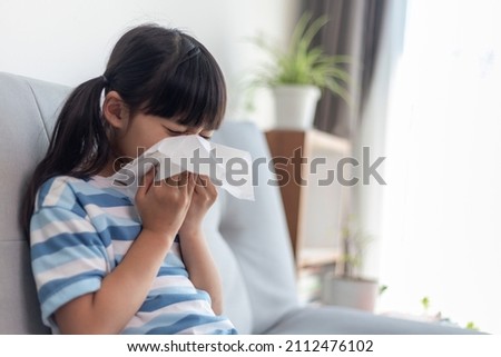 Unhealthy kid blowing nose into tissue, Child suffering from running nose or sneezing, A girl catches a cold when season change, childhood wiping nose with tissue Royalty-Free Stock Photo #2112476102
