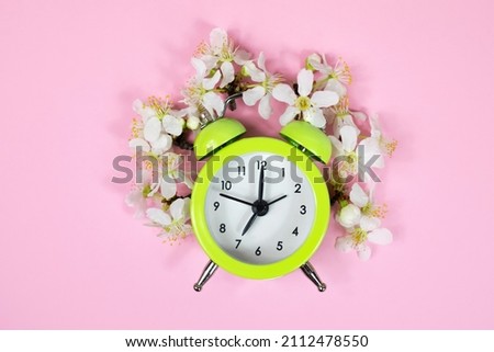 Vintage green alarm clock and natural cherry flowers on a pink background. Flat lay, space for text.