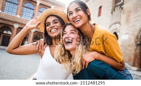 Three young multiracial women having fun on city street outdoors - Mixed race female friends enjoying a holiday day out together - Happy lifestyle, youth and young females concept Royalty-Free Stock Photo #2112481295