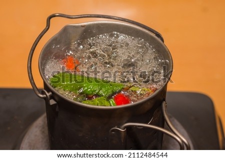 boiling survival tea with rose hips and leaves with many bubbles with orange background
