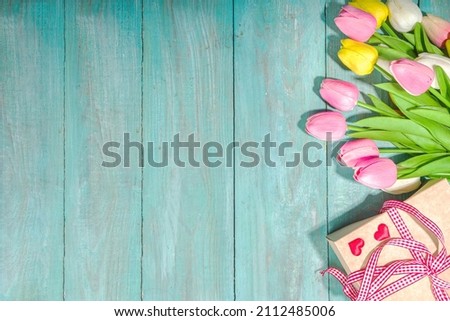 Spring holiday greeting card background with various color tulip flowers, gift box, flatlay on light blue high-colored wooden background top view copy space