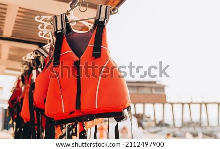 Life jacket on rail for costumer, Red Life jacket with black belts, Personal flotation device. Life jacket ready to be used by tourist going on a boat trip. Royalty-Free Stock Photo #2112497900