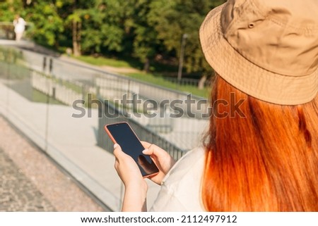 Mockup image of hand holding mobile phone with blank screen. Girl use smart phone share social media news wear style stylish trendy hat over city background, Summer time