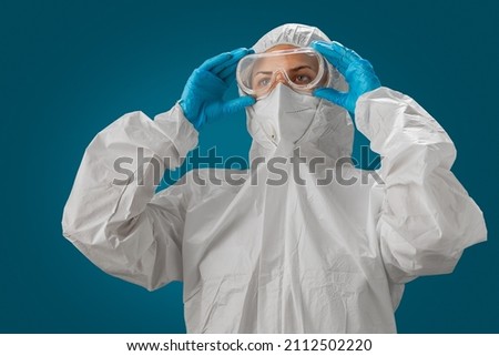 Scientist or Medical staff wearing personal protective gown or PPE, white N95 mask and blue medical gloves puts on goggles. Personal protective equipment to protect against coronavirus covid-19. Royalty-Free Stock Photo #2112502220