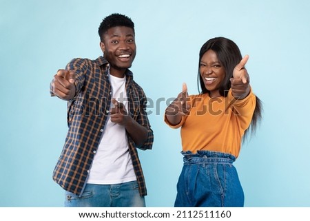 Hey, You. Portrait of cheerful African American guy and lady pointing two index fingers at camera, standing isolated over blue studio background wall. Positive young friends choosing and indicating Royalty-Free Stock Photo #2112511160