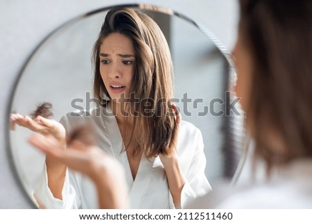 Hairloss Concept. Worried Young Woman Holding Bunch Of Fallen Hair In Hand While Standing Near Mirror In Bathroom, Stressed Beautiful Lady Suffering Alopecia Or Health Problems, Selective Focus Royalty-Free Stock Photo #2112511460