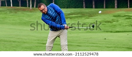 Golfer on a golf course in winter with wet grass, hitting the ball with a golf club.