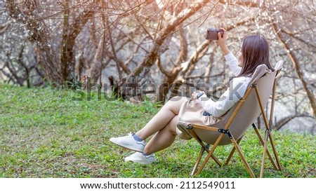 beautiful girl sit back and relax on the chair have a camera in  hand.under the tree on a sunny day, selective focus ,Relaxion concept.