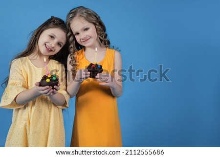 Two girls with cupcakes and festive candles on a bright backgrou