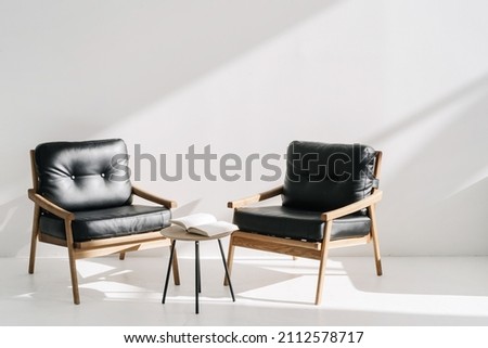 Two minimalistic leather armchairs standing near coffee table in luxury office or bright stylish apartment. Open book, agenda or planner in meeting room at business center Royalty-Free Stock Photo #2112578717