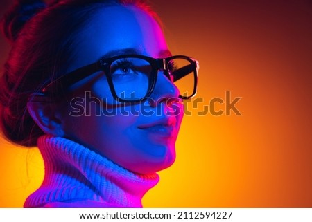 Looks calm, confident. Closeup young beautiful girl in eyewear isolated on orange background in neon light, filter. Concept of emotions, facial expression, youth, aspiration, sales. Copy space for ad