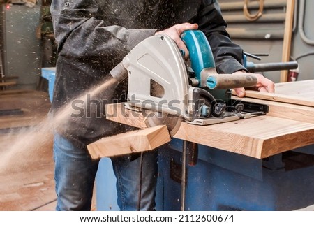 Male carpenter sawing a board with a circular saw in a carpentry workshop close-up Royalty-Free Stock Photo #2112600674