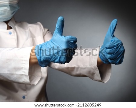 female wearing mask doctor's hands in nitrile blue gloves show the test okay thumbs up