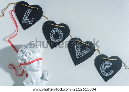 Festive background for Valentine's Day with black hearts with the inscription Love male bust with a red ribbon on the eyes on a white background. Layout with copy space for design.
