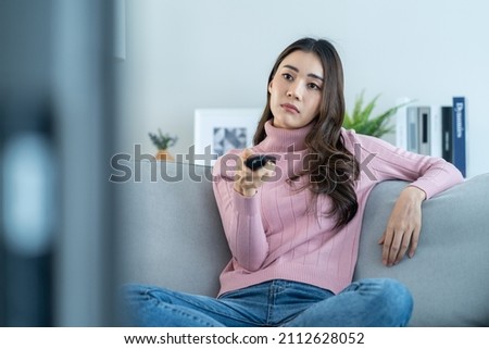 Asian unhappy young beautiful woman watch movie on television at home. Attractive girl feel upset, sit on sofa in living room watch video on TV with boring face in house. Activity lifestyles concept.