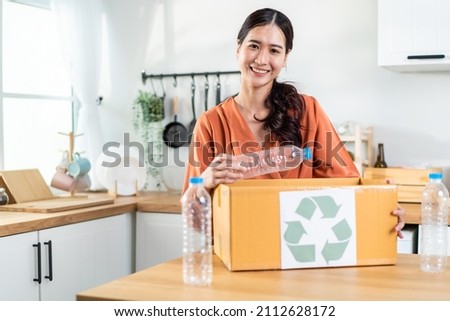 Portrait of Asian woman hold trash bin for further recycling at home. Attractive female put plastic bottles into recycle box for ecologically friendly and saving the environment. Zero waste concept.