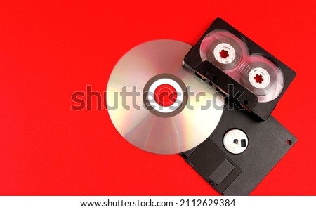 Audio cassette, floppy disk and disc on a red background. Legacy technologies