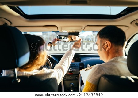 Close up of female hands correcting mirror. Traveler girl on car trip, looking at the road. View over shoulder Female on test drive car with instructor Royalty-Free Stock Photo #2112633812