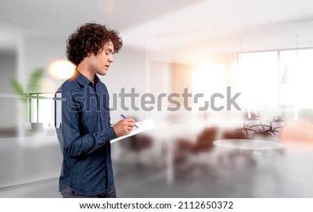 Businessman in denim shirt, profile, writing in business papers with pen, concentrated look. Concept of business student. Company workplace with modern furniture
