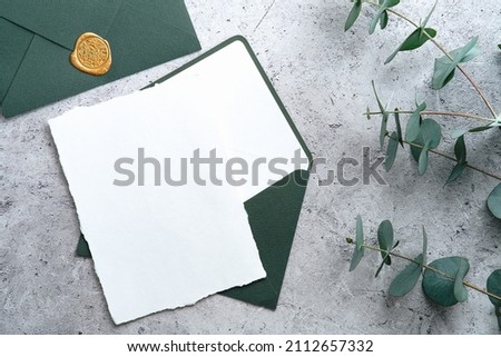 Wedding stationery set. Wedding invitation card template, green envelope, eucalyptus branches on concrete background. Flat lay, top view, copy space.