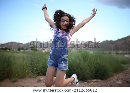 happy little girl jumping with arms wide open outdoors