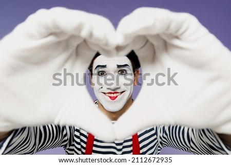 Close up happy young mime man with white face mask wears striped shirt beret showing shape heart look through hands heart-shape sign isolated on plain pastel light violet background studio portrait