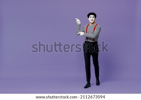Full size happy young mime man with white face mask wears striped shirt beret point finger aside on workspace area copy space mock up isolated on plain pastel light violet background studio portrait