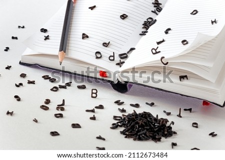 a lot of small black Latin letters scattered across the pages of a notebook and a table, the concept of grammar and spelling, creativity and ideas for a story Royalty-Free Stock Photo #2112673484