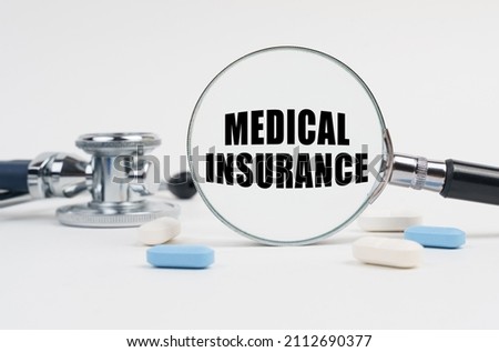 Medicine and health concept. On a white surface lie pills, a stethoscope and a magnifying glass with the inscription - Medical Insurance