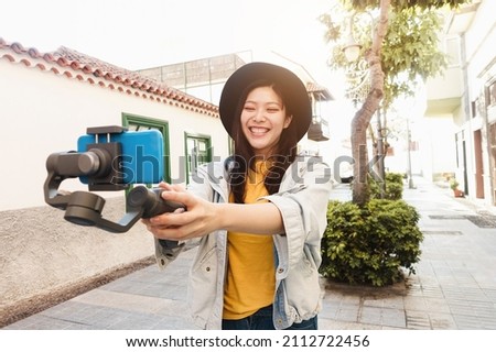 Happy asian influencer having fun vlogging with gimbal and mobile phone outdoor - Focus on face Royalty-Free Stock Photo #2112722456