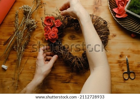 Valentines day DIY decoration, spring home decor crafts. Female hands decorates heart shaped floral wreath. 