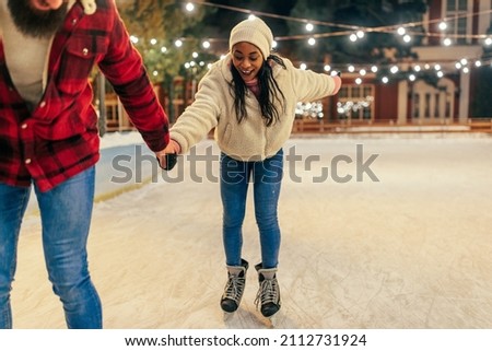 Happy biracial couple holding hands while ice skating together.