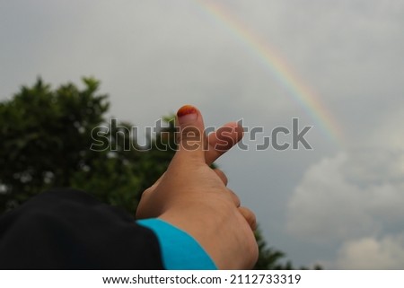 Hand making a love sign with rainbow background on a cloudy sky after rain in the afternoon. Happy, Love and peace concept background