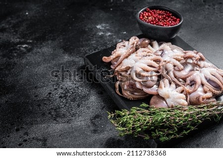 Raw mini baby octopus on a marble board with thyme. Black background. Top view. Copy space